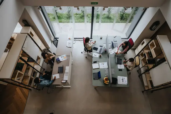 由一组专业人员与计算机和讨论一起在办公桌前工作的明亮的开放式办公室的俯拍 — 图库照片