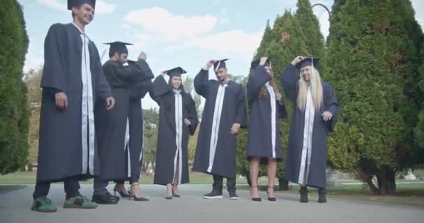 在阳光灿烂的公园里 身着帽子和长袍的毕业生们把帽子抛向空中 庆祝他们的成就 分享快乐 共同编织美好的回忆 — 图库视频影像