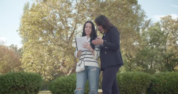 在一个公园里 两名年轻的女大学生进行了认真的讨论 讨论的重点反映了她们共同的学术兴趣 或在一片繁茂的环境中交流个人故事 — 图库视频影像