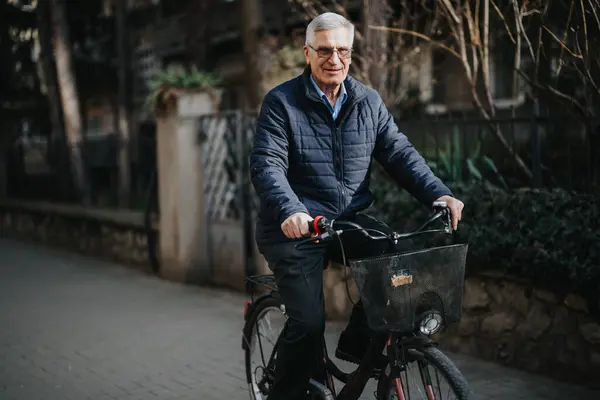 活気あふれる高齢の紳士が自転車に乗りながら自信を持って笑顔を浮かべ 都会の背景から健康で活発なライフスタイルを披露します — ストック写真
