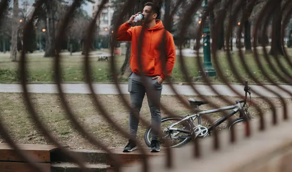 屋外の公園で自転車に乗って曇った日に水分補給する若い男 — ストック写真