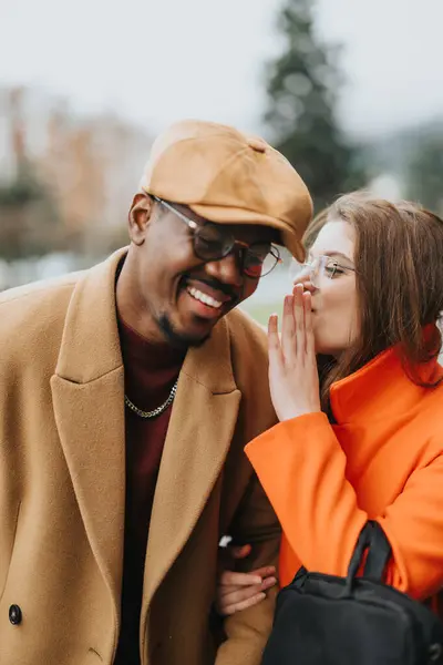 stock image Elegant multiracial business partners enjoy a light-hearted moment while walking on a cloudy day, as the woman whispers into the mans ear.