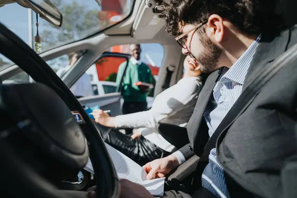 Professional business people in formal wear engaged in a conversation inside a vehicle with paperwork in hand.