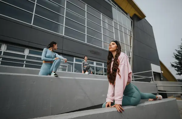 3名身穿运动服的年轻女子在一座现代建筑旁的城市健身活动中暂停休息 — 图库照片