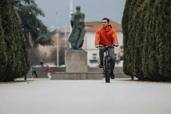 赤いパーカーの若い男は 荒天の公園のパスに自転車に乗っています — ストック写真