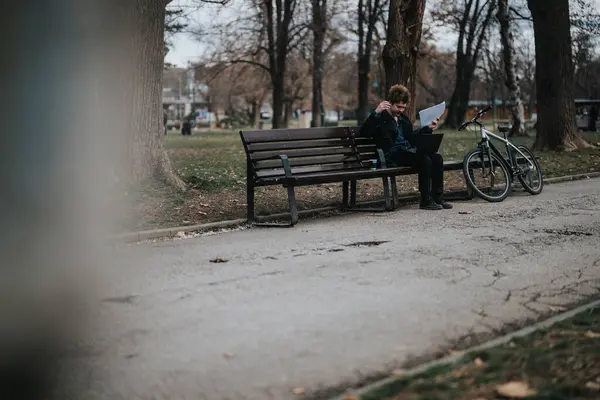 一位企业家在公园里享受着宁静的时光 他坐在一条长椅上 身边有一台笔记本电脑和一辆自行车 — 图库照片