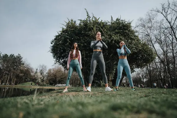 Three female athletes stretching and warming up in a sunny park environment, showcasing a healthy lifestyle
