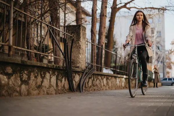 A young woman pedals confidently down a city street, displaying a sense of freedom and urban exploration while enjoying a casual bike ride.