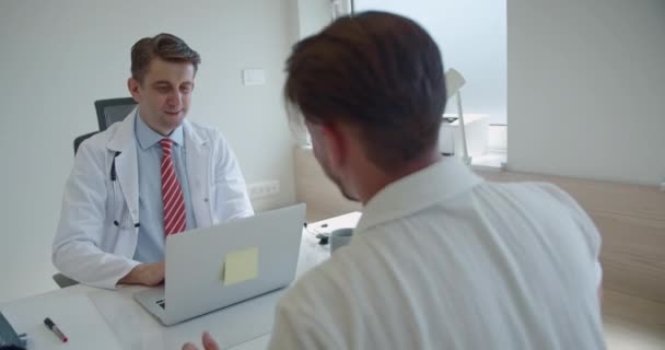 Zkušený Lékař Pracuje Laptopu Pečlivě Naslouchá Svému Mladému Pacientovi Vysvětluje — Stock video