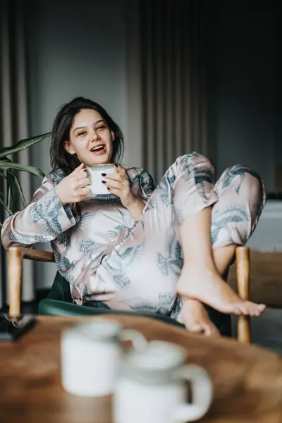 A calm and serene woman sitting comfortably in pajamas, savoring a warm beverage at home.