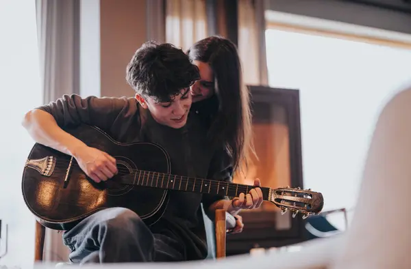 愛するカップルは 音楽的な情熱の瞬間を密接に共有し 女性が後ろから彼を受け入れるようにギターを演奏する男性は 両方の家で — ストック写真