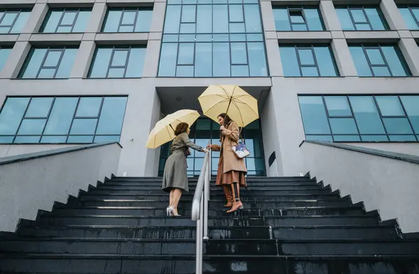 Dwie Profesjonalistki Żółtymi Parasolkami Opuszczające Nowoczesny Biurowiec — Zdjęcie stockowe