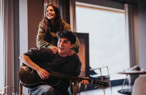 男がギターを弾いている男と 彼の後ろに立っている女性と一緒に家で楽しいカップル 笑顔と楽しい時間を過ごす — ストック写真