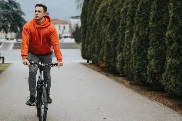 カジュアルな服装の若者は曇った日に屋外で自転車に乗り 公園の静けさを楽しみます — ストック写真