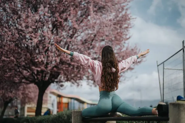 在一个宁静的公园里 一位宁静的年轻女子在盛开的樱桃树间摆出瑜伽姿势 — 图库照片