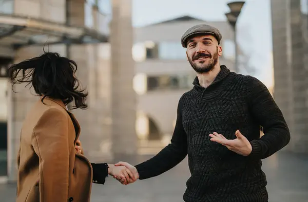 A cheerful man in a sweater and cap is holding hands with a woman in a coat, walking and chatting in a city environment, conveying a sense of happiness, love, and companionship.