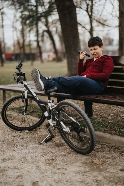 Radosny Młody Chłopiec Siedzi Ławce Parku Rowerem Przy Sobie Robi — Zdjęcie stockowe
