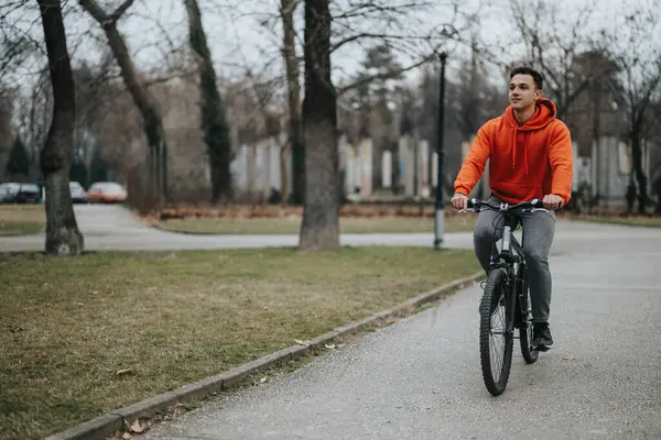 赤いパーカーの若い男は静かな公園を通って自転車に乗り 天気は平和な屋外の設定に追加されます — ストック写真