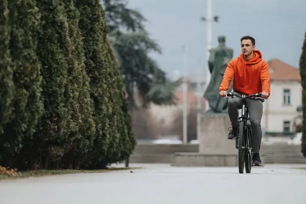 赤いフーディーの若い男は 天空の下の静かな公園の設定を介して自転車に乗る — ストック写真