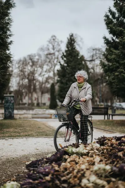 An independent mature woman leisurely cycling through a tranquil park setting, embracing an active lifestyle.