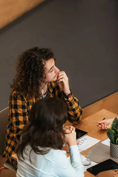 让卷发女人穿着格子衬衫参加商务会议 带着若有所思的表情 与同事讨论图表和策略 — 图库照片