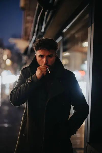 一位英俊的商人站在繁忙的城市人行道上 一边抽烟一边在雨夜等出租车 下班以后 他将回城市 — 图库照片