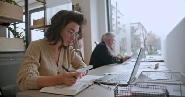 ビジネスウーマンは現代のオフィスで彼女の机で働き 共同精神で彼女の仕事に魅了され チーム全体の成功に貢献します — ストック動画