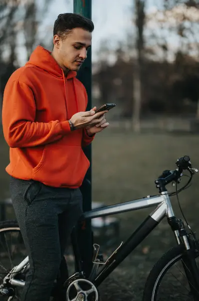 スマートフォンを使って静かな都市公園で自転車で休むカジュアルな若者 — ストック写真