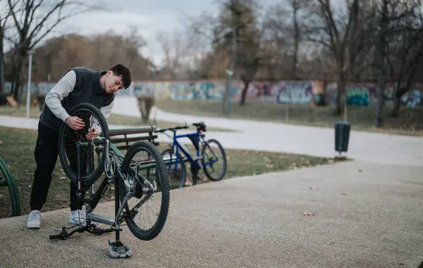 在室外公园里修理自行车轮子的男青年 — 图库照片