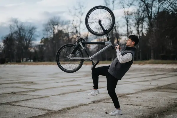 Casual male teenager performs a bicycle stunt in a peaceful park setting, displaying youth and skill.
