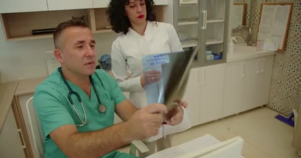 Starszy Lekarz Młoda Pielęgniarka Analizują Omawiają Zdjęcie Rentgenowskie Pacjenta Gabinecie — Wideo stockowe