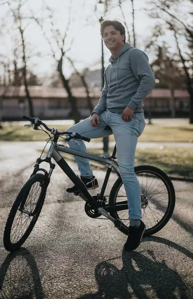 A smiling young adult male posing with his bike in a park setting, exuding a carefree and healthy lifestyle vibe.