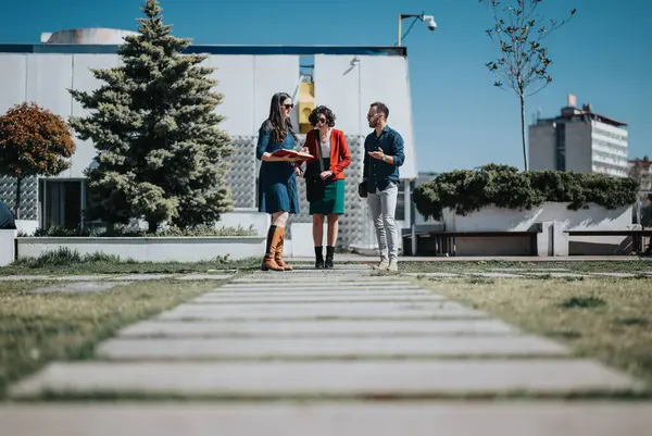 Three business professionals engaged in a meeting while standing outdoors on a sunny day.