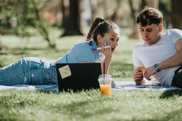 Two high school students engaged in studying and helping each other with homework while relaxing in an urban park setting.