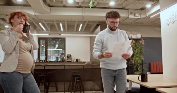 在现代化的办公室里 怀孕的女商人一边喝茶 一边和男同事一起复习文书工作 — 图库视频影像