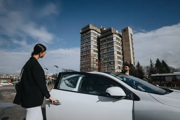 スタイリッシュな黒いコートのエレガントな女性は 都市建築の背景に彼女の白い車を運転する準備ができています — ストック写真
