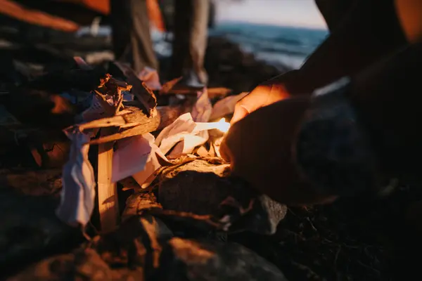 Snug Scene Showing Hands Lighting Fire Amidst Crumpled Papers Seaside — Stock Photo, Image