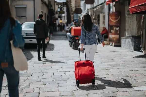 Young Woman Striped Shirt Pulls Red Suitcase Vibrant Cobblestone Street — Stock Photo, Image