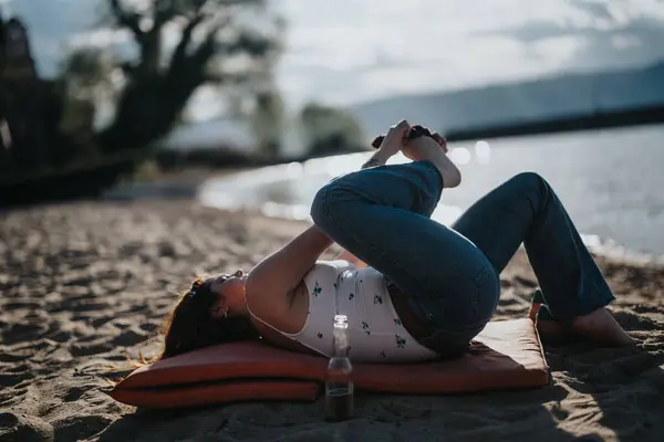 A peaceful scene as a young woman enjoys yoga on a sunlit beach, capturing the essence of relaxation and solitude by a serene lake.
