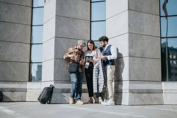 Three young professionals engage in a business meeting outside a modern urban building, focused on collaboration and planning.