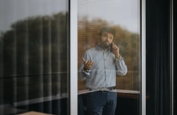 現代のオフィスの窓の隣で電話で会話に従事したプロのビジネスマン 自信と成功を除く ストックフォト