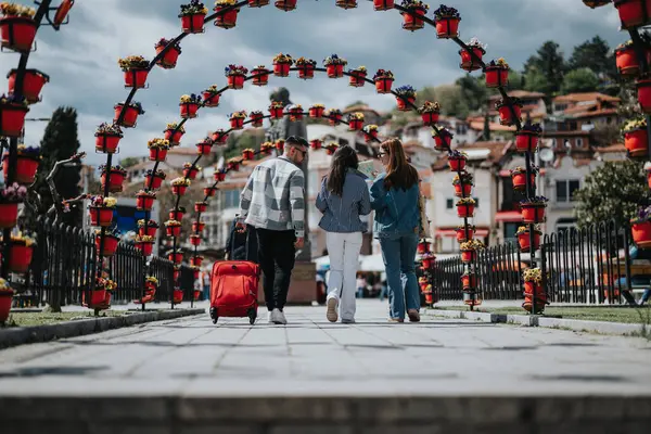 Young Couple Suitcase Friend Walking Vibrant Flower Filled Arches Scenic — Stock Photo, Image