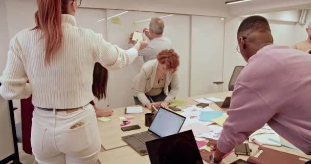 一个协作小组参加一个集思广益会 利用贴纸在明亮的办公室空间分享想法和制定项目战略 — 图库视频影像