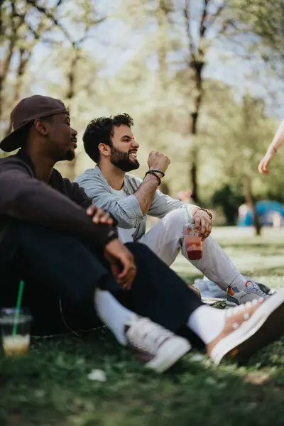 Two Multiracial Friends Sitting Park Laughing Chatting Drinks Hand Enjoying Fotografias De Stock Royalty-Free