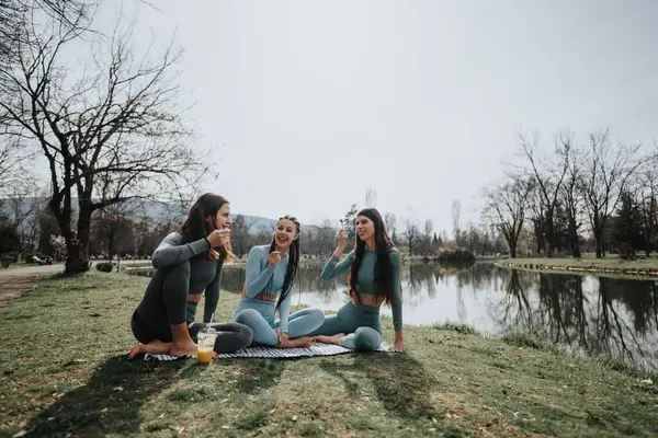 3人の友人が水辺の穏やかな公園で一緒にヨガを練習し フィットネスと友情を示しています ロイヤリティフリーのストック写真