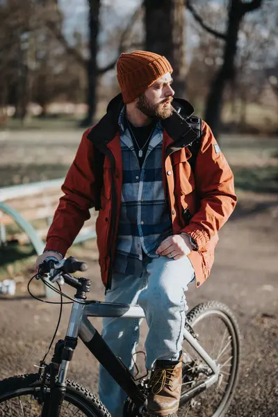 ビーニーとジャケットを着た髭の男の屋外の肖像画は 秋の間に公園で自転車で立っています — ストック写真