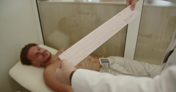 Médico Experimentado Leyendo Revisando Analizando Electrocardiograma Mientras Examina Paciente Joven — Vídeos de Stock