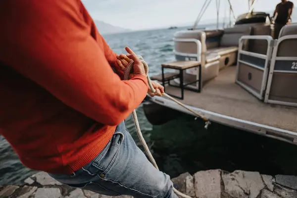 Close-up of a persons hands tying a rope while securing a boat to a dock, showcasing a nautical theme.