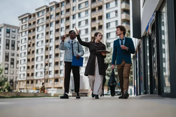 Multiracial business team actively engaged in a discussion while walking through an urban area with modern architecture in the background.