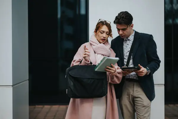 stock image Two young entrepreneurs or colleagues engaged in a strategic business discussion while reviewing data on a tablet, outdoors in a city area.